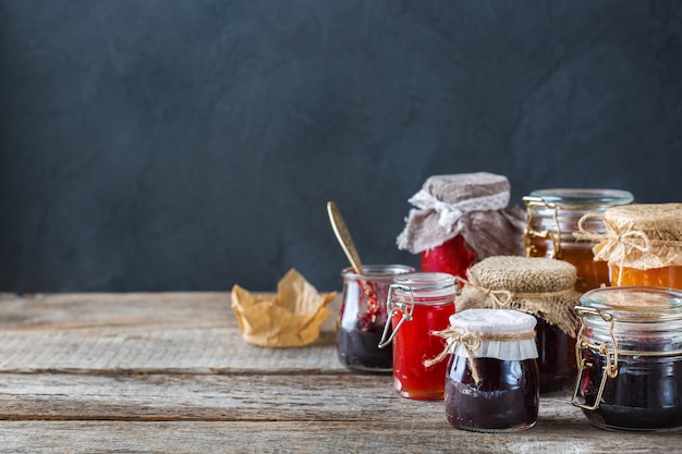 Cibo e bevande, raccolto estate autunno concetto. Assortimento di frutti di bosco e marmellate di frutta stagionali in barattoli su un tavolo di legno. Copia spazio sfondo rustico