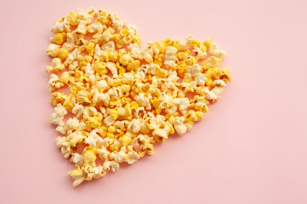 Cibo. Immagine delle forme di cuore da popcorn. Popcorn delizioso sul rosa. Cinema.