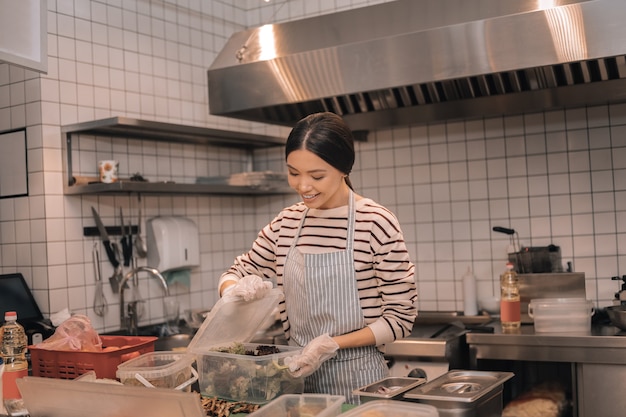 Cibo in contenitori. Utile lavoratore dai capelli scuri della cucina che mette il cibo nei contenitori