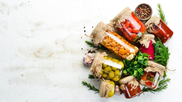 Cibo in scatola in vasetti di vetro su fondo di legno bianco Verdure sottaceto e funghi