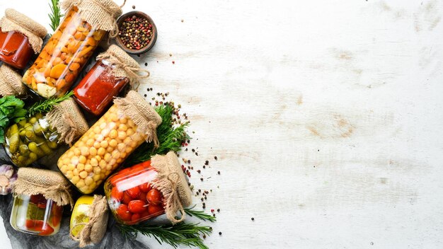 Cibo in scatola in vasetti di vetro su fondo di legno bianco Verdure sottaceto e funghi