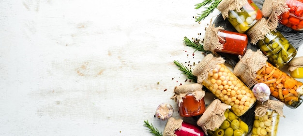 Cibo in scatola in vasetti di vetro su fondo di legno bianco Verdure sottaceto e funghi