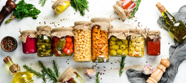 Cibo in scatola in vasetti di vetro su fondo di legno bianco Verdure sottaceto e funghi