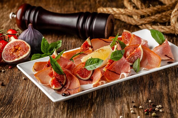 Cibo italiano. Antipasti antipasto con prosciutto, fichi e basilico. Serve piatti in un ristorante in un piatto bianco su un tavolo di legno