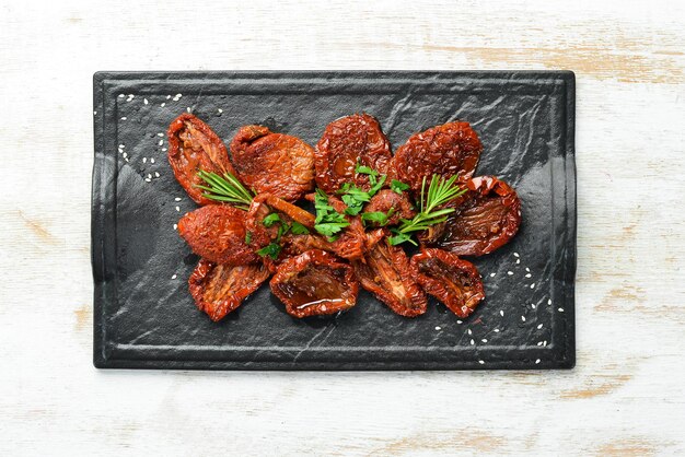 Cibo italiano Pomodori essiccati al sole con erbe e spezie fresche su una lastra di pietra nera Vista dall'alto