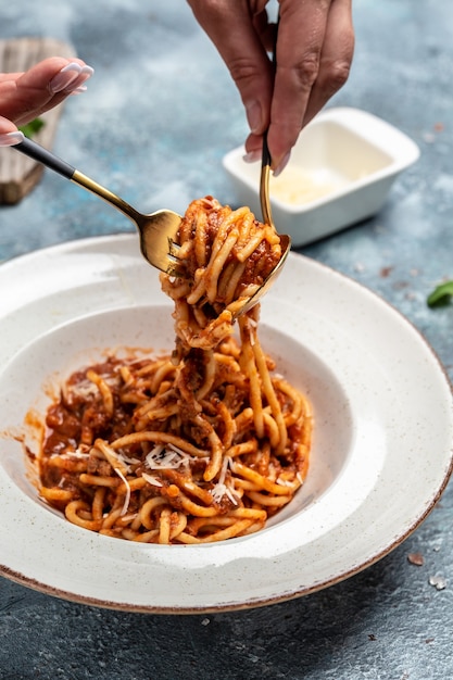 Cibo italiano. Spaghtti di pasta al pomodoro e sugo di carne macinata serviti in un piatto con parmigiano sulla forcella. immagine verticale.