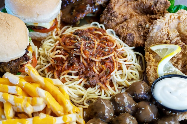 Cibo malsano Spaghetti, bistecca, pollo fritto, hamburger, patatine fritte e polpetta di carne su una grande ciotola