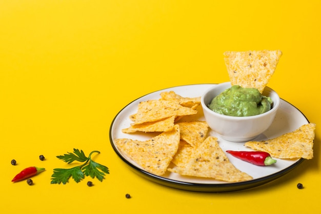 Cibo messicano Guacamole tuffo con chips di mais su sfondo giallo.