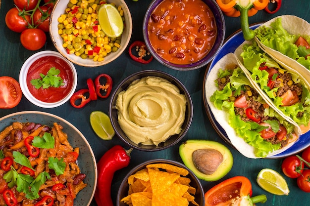 Cibo messicano misto. Cibo per feste. Guacamole, nachos, fajita, tacos di carne, salsa, peperoni, pomodori su un tavolo di legno. Vista dall'alto.