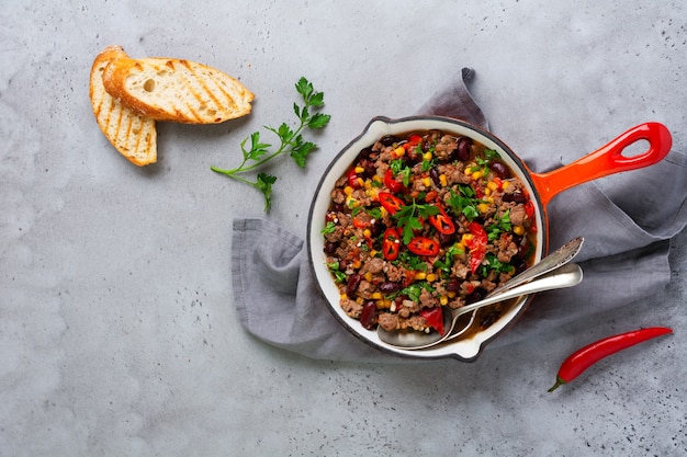 Cibo messicano tradizionale - Chili con carne con carne macinata e verdure stufate in salsa di pomodoro in una padella di ghisa su ardesia grigio chiaro o sfondo di cemento. Vista dall'alto con copia spazio