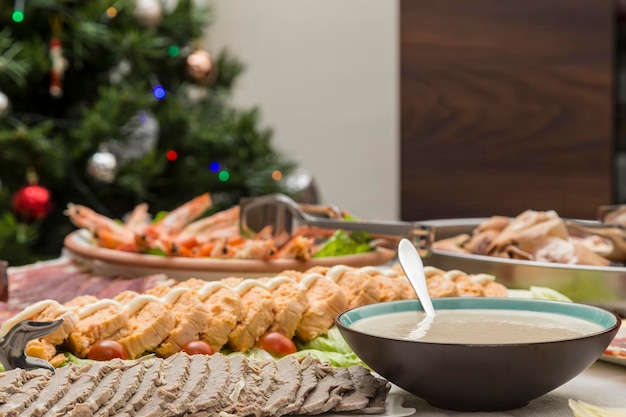 Cibo natalizio preparato in un abbondante buffet carne tritata una salsa torta di pesce gamberi frutti di mare affettati sullo sfondo l'albero con i suoi ornamenti