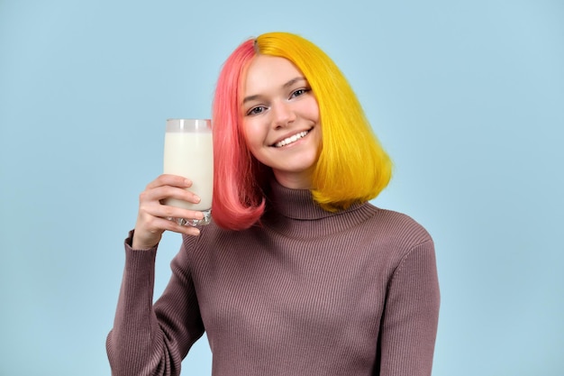 Cibo naturale sano, bicchiere di latte in mano di un bellissimo modello adolescente sorridente, su sfondo blu per studio