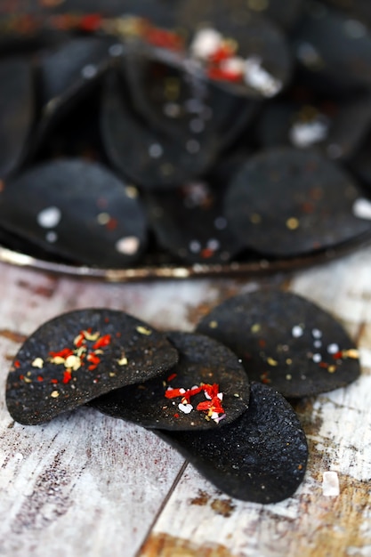 Cibo nero. Chip neri con le spezie su una zolla. Tendenza del cibo nero.