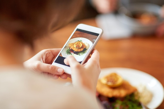 cibo, nuova cucina nordica, tecnologia, alimentazione e concetto di persone - donna con smartphone che fotografa filetto di pesce impanato con salsa tartara e insalata di pomodoro barbabietola al forno al ristorante