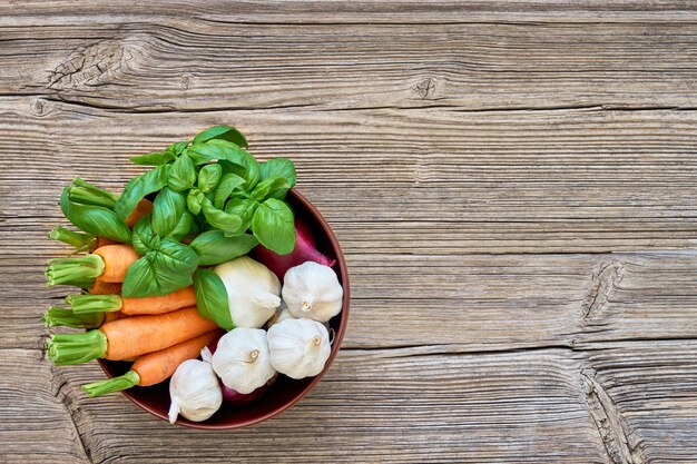 Cibo organico. Carote, aglio e basilico nella ciotola su fondo di legno.