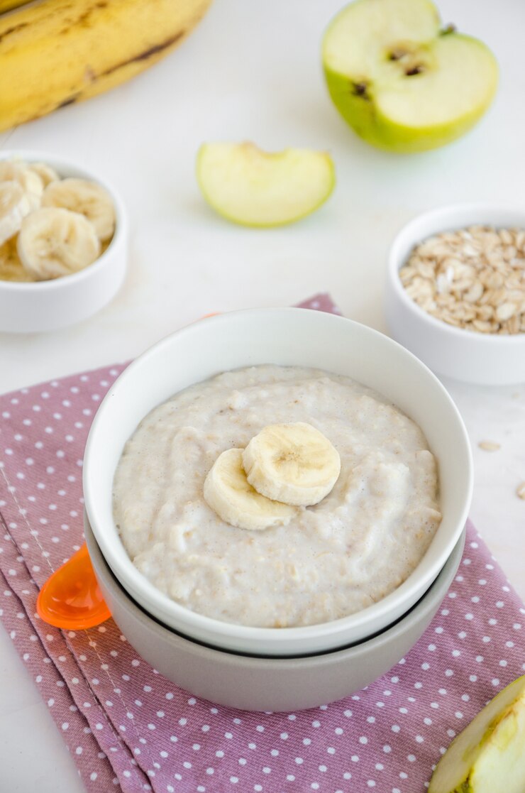 Foto cibo per bambini. farina d'avena cremosa con fette di banana e mela in una ciotola con un cucchiaio su uno sfondo chiaro. colazione salutare. porridge per colazione.