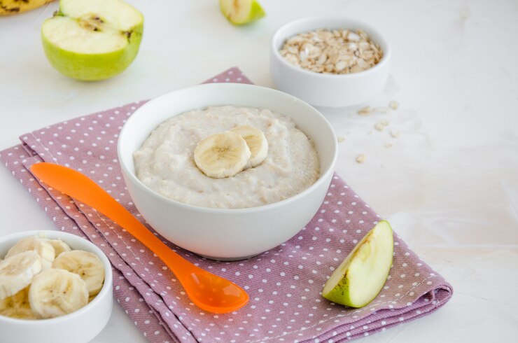 Foto cibo per bambini. farina d'avena cremosa con fette di banana e mela in una ciotola con un cucchiaio su uno sfondo chiaro. colazione salutare.