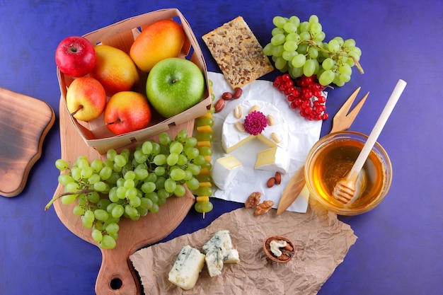 Cibo per uno spuntino sano e gustoso su sfondo viola Camembert con frutti di bosco, miele e noci su una tavola di legno Primo piano