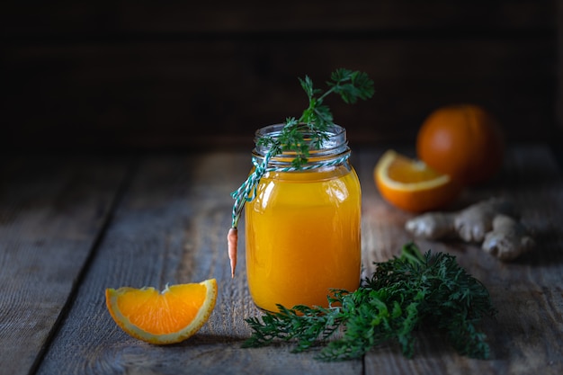 Cibo salutare. Carote e succo di carota con zenzero arancione in un barattolo di vetro in un cestino di metallo su una superficie di legno scuro