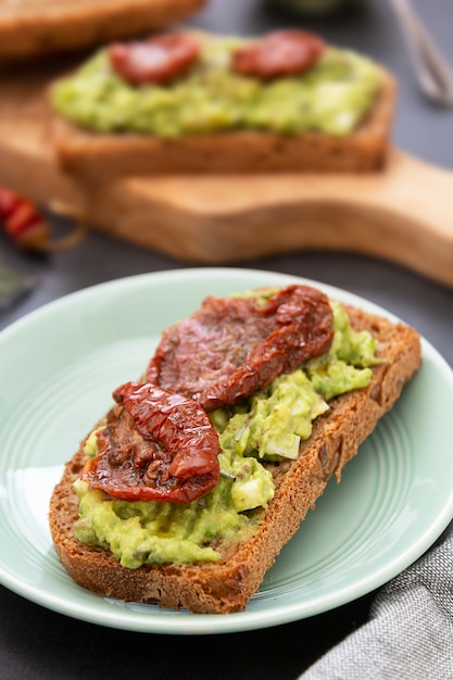 Cibo salutare. Pane di segale con guakomole, pasta di avocado e pomodori secchi, sul tagliere di legno. Toast all'avocado.