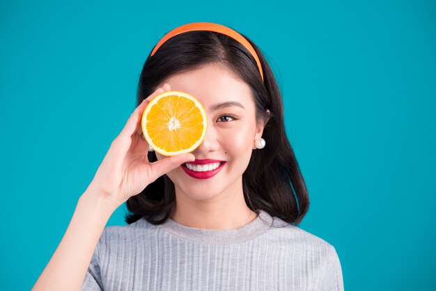 Cibo salutare. Sorridente bella ragazza asiatica del pinup che tiene arancia su sfondo blu.