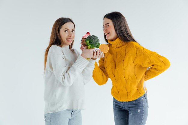 Cibo salutare. Una donna tiene in mano dei broccoli e l'altra una torta