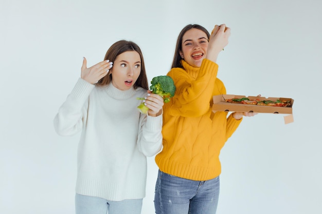 Cibo salutare. Una donna tiene in mano una pizza e l'altra un broccolo