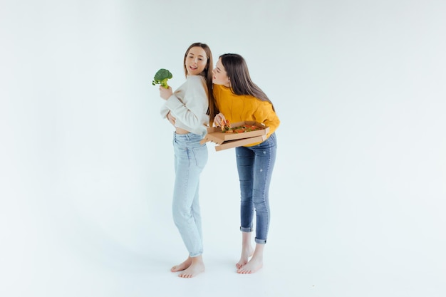 Cibo salutare. Una donna tiene in mano una pizza e l'altra un broccolo