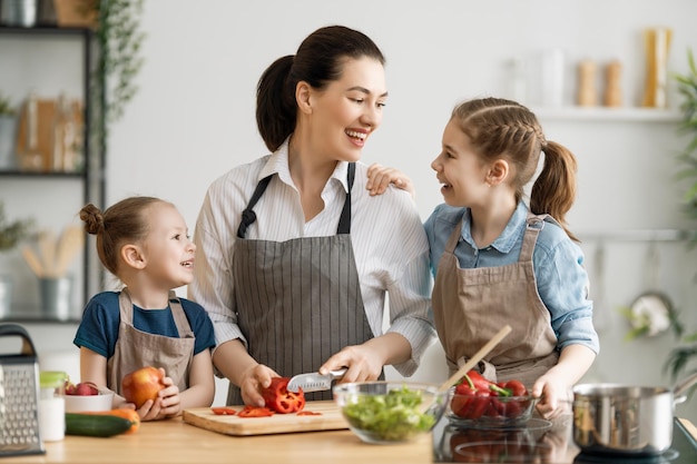 Cibo sano a casa. Famiglia felice in cucina. Le figlie dei bambini e della madre stanno preparando le verdure.