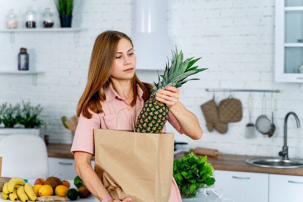 Cibo sano a casa. La donna felice sta mostrando l'ananas in cucina moderna. Stile di vita vegano e vegetariano.