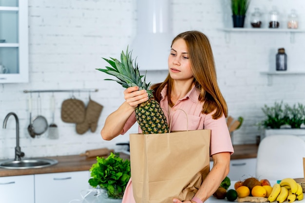 Cibo sano a casa La donna felice sta mostrando l'ananas nella cucina moderna Vita vegana e vegetariana