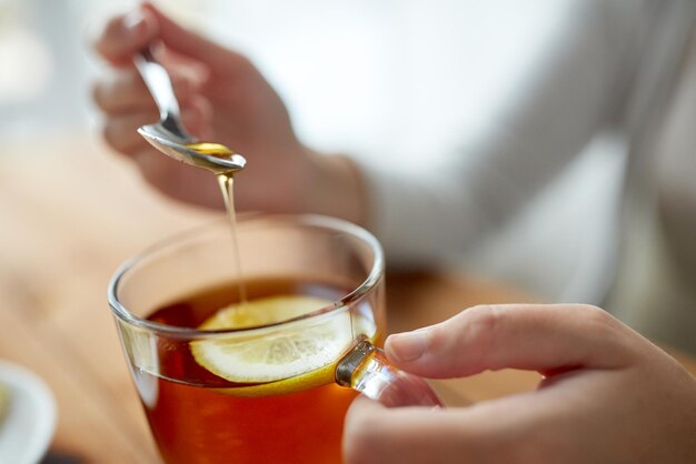 cibo sano, alimentazione e concetto di etnoscienza - primo piano della donna che aggiunge miele alla tazza di tè con il limone