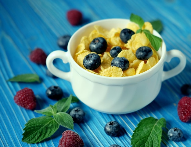 Cibo sano e concetto di dieta Fiocchi di mais con bacche di lamponi e mirtilli su sfondo di legno blu