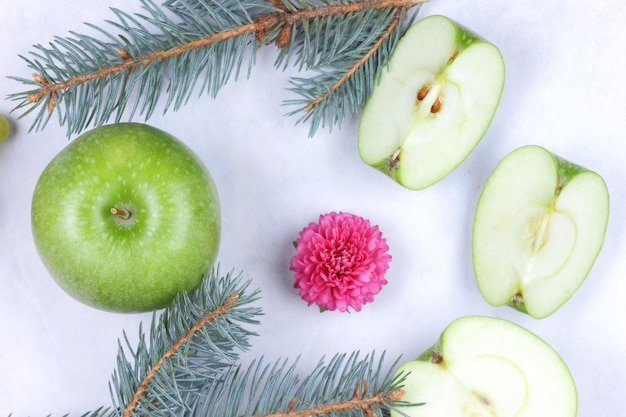 Cibo sano e concetto di stile di vita Mela succosa verde matura e pezzi di mela con rami di abete su sfondo chiaro Primo piano