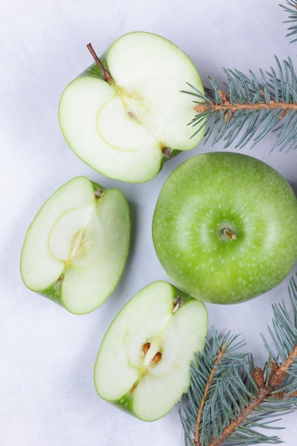 Cibo sano e concetto di stile di vita Mela succosa verde matura e pezzi di mela con rami di abete su sfondo chiaro Primo piano