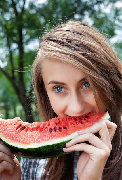 Cibo sano e concetto di stile di vita sano. La giovane donna felice sta mangiando la fetta di anguria