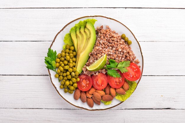 Cibo sano Grano saraceno pomodorini avocado mandorle e piselli su sfondo di legno Vista dall'alto Spazio libero per il testo