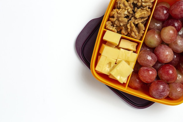 Cibo sano in contenitori di plastica pronti da mangiare con formaggio, uva e noci sul tavolo di lavoro