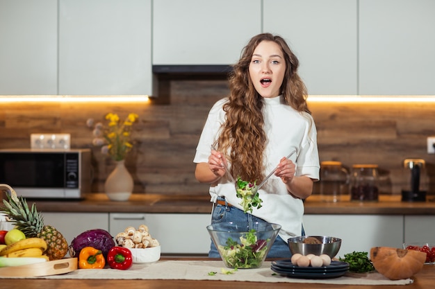 Cibo sano - Insalata di verdure. Dieta. Concetto Dieta. Giovane donna riccia che prepara insalata di verdure nella sua cucina. Concetto di stile di vita sano, bella donna mista emotiva, sorpresa donna.