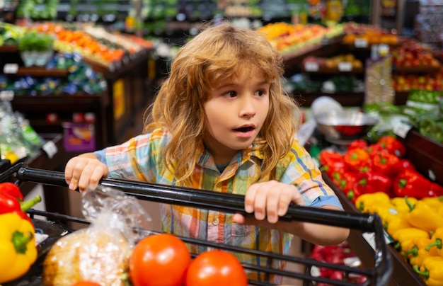 Cibo sano per giovani famiglie con bambini Ritratto di bambino sorridente con carrello pieno di verdure fresche Bambini al negozio di alimentari o al supermercato Concetto di negozio di alimentari del carrello della spesa