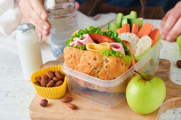 Cibo sano per il concetto di pranzo a scuola Padre di cura che prepara il pranzo a scuola Panino con pane sano carne formaggio mele cetrioli carote noci acqua yogurt nel contenitore Ritorno al concetto di scuola