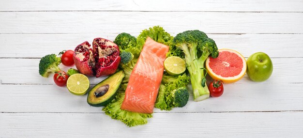 Cibo sano Pesce salmone avocado broccoli verdure fresche noci e frutta Su uno sfondo di legno bianco Vista dall'alto Spazio di copia