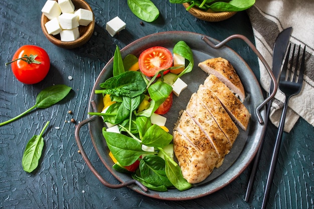 Cibo sano Pranzo dietetico chetogenico Filetto di pollo alla griglia con insalata di verdure fresche, spinaci e feta su uno sfondo di pietra scura