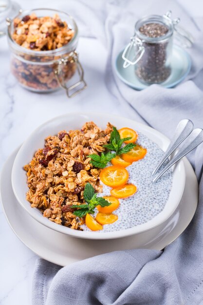 Cibo sano vegetariano biologico e concetto di cibo dietetico Ciotola per budino di chia vegano con granola fresca fatta in casa, kumquat arancione e menta verde per colazione