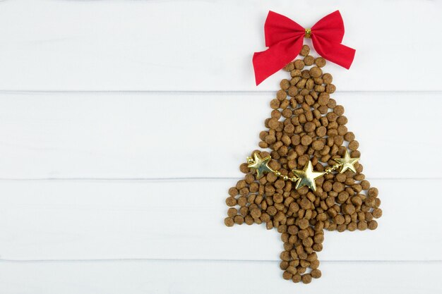 Cibo secco per cani Albero di Natale con fiocco rosso sulla parte superiore e ghirlanda. Concetto di forniture per animali domestici di Natale