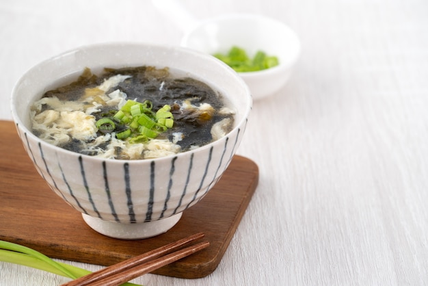 Cibo taiwanese - zuppa di uova di alghe deliziosa fatta in casa in una ciotola su un vassoio da portata su sfondo di tavolo in legno chiaro.