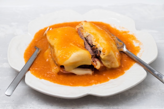 Cibo tipico portoghese Francesinha in piatto bianco con forchetta e coltello