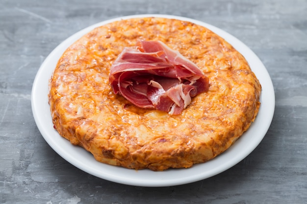 Cibo tipico spagnolo Tortilla con carne affumicata e patate sul piatto bianco