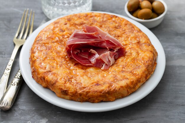 Cibo tipico spagnolo Tortilla con carne affumicata e patate sul piatto bianco