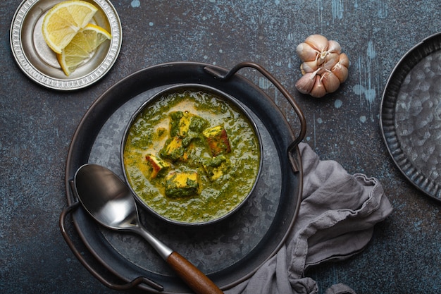 Cibo tradizionale indiano Punjabi Palak Paneer con spinaci e formaggio in una ciotola di metallo vintage con cucchiaio su sfondo rustico in cemento dall'alto